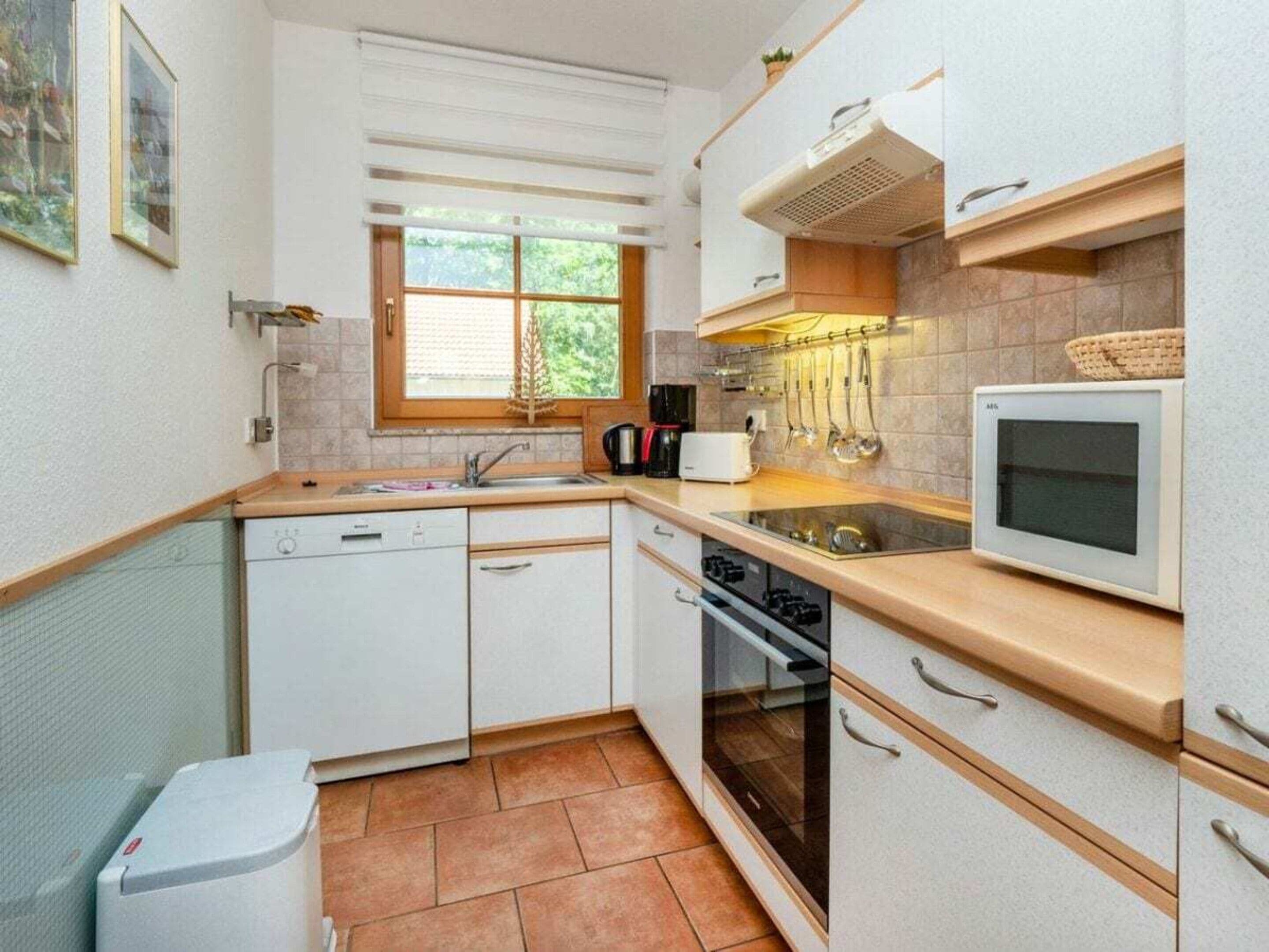Eine kompakte Küche mit Geschirrspüler, Backofen, Mikrowelle und einem Fenster für natürliches Licht.