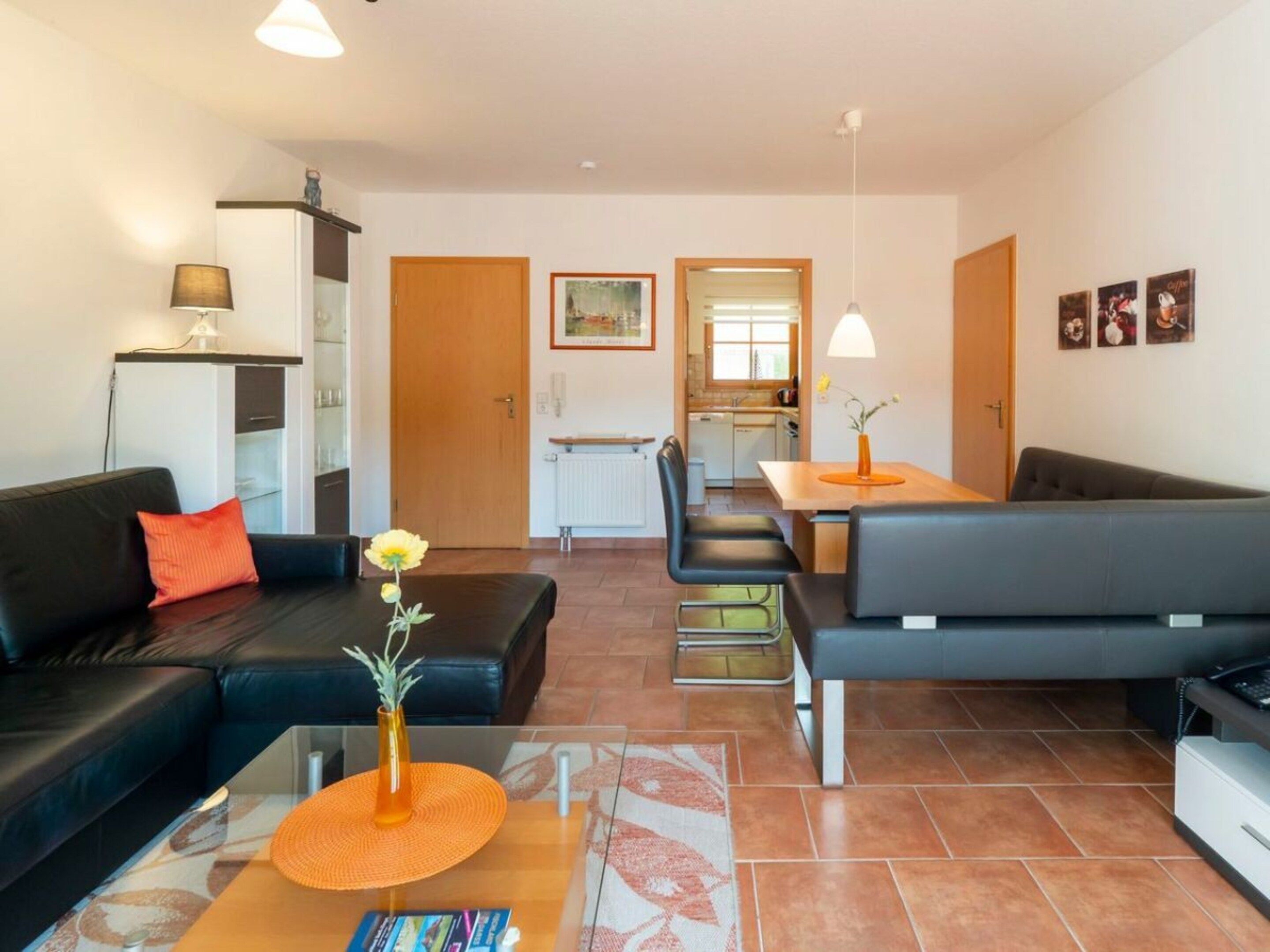 A modern living room with a sofa, a coffee table with a vase, and a dining area with a table and chairs.