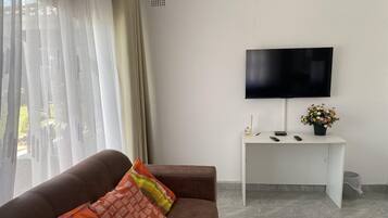 Ein Wohnzimmer mit einem braunen Sofa, einem weißen Schreibtisch, einem Flachbildfernseher und einer Topfpflanze.