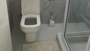 Ein Badezimmer mit Toilette, einer Duschkabine aus Glas und einem Marmorboden.