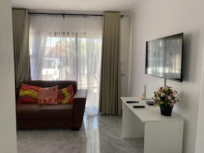 Ein modernes Wohnzimmer mit einer Couch, einem Flachbildfernseher, einem Schreibtisch und einem Topfpflanzen.