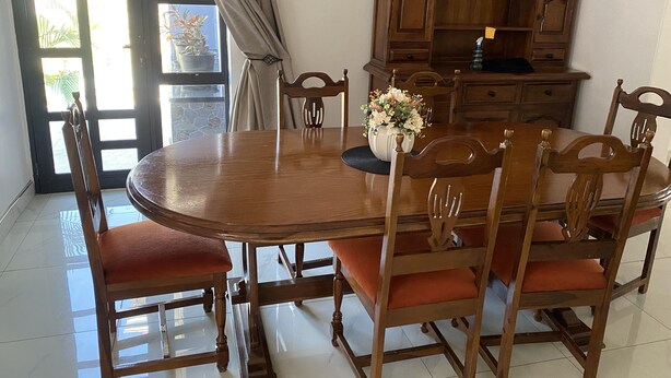 Un coin repas comprenant une table en bois, des chaises, un vase avec des fleurs et un meuble en bois.
