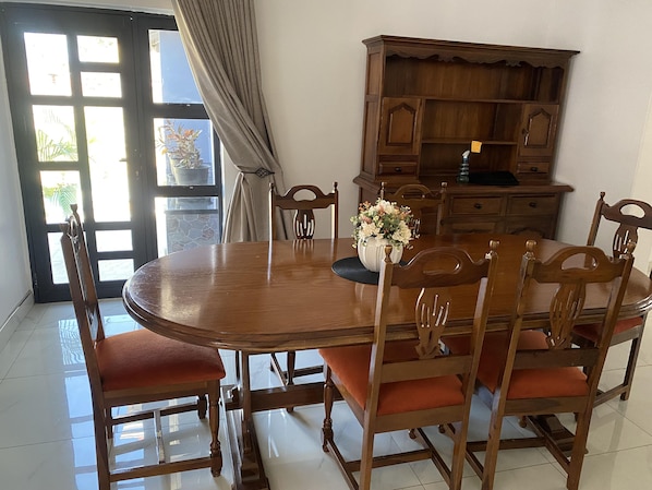 Un comedor con mesa de madera, sillas, un jarrón con flores y un armario de madera.