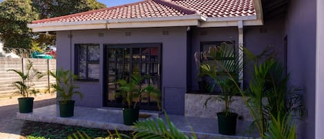 Una casa con techo de tejas, plantas en macetas y camino de entrada pavimentado.