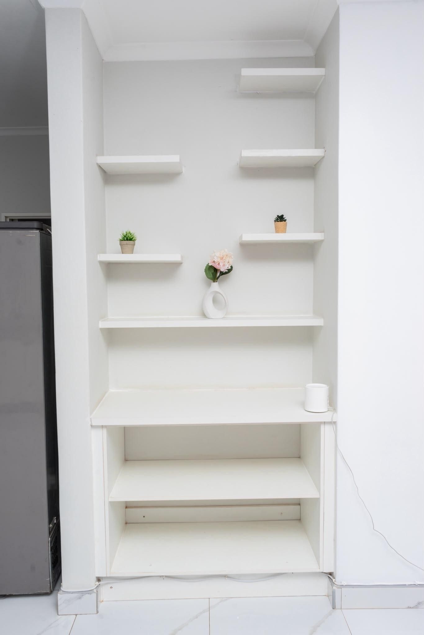 A white interior with a built-in shelf unit against a wall, a small potted plant, and a vase with flowers.