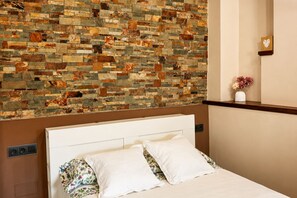 A hotel room with a bed, a headboard, a wall with a mosaic design, a small shelf with a vase, and a heart-shaped decoration. - Can Costals Cerezo in Pals (Els Masos de Pals)