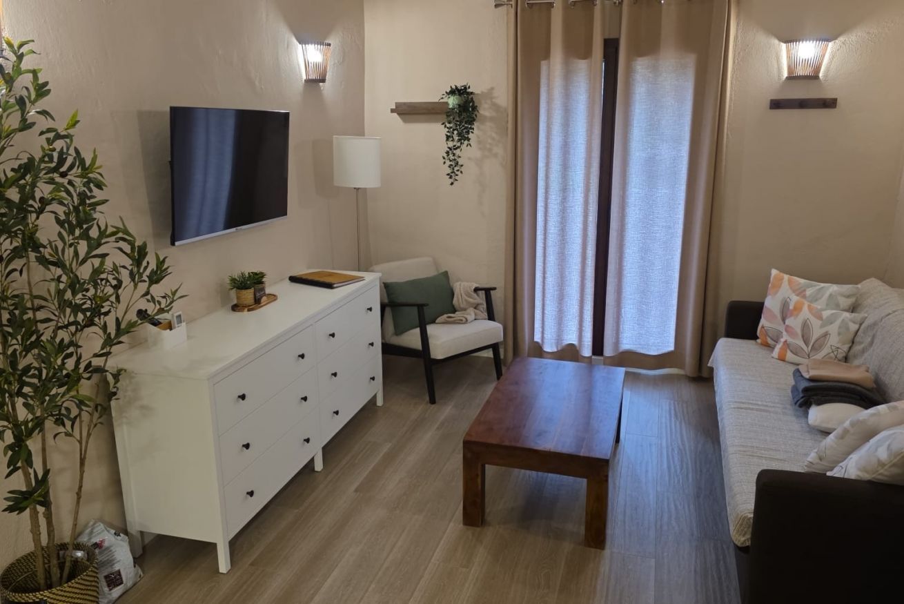 A living room with a flat-screen TV, a white cabinet, a wooden table, a sofa, and a chair.