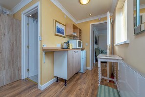 A compact kitchen with a microwave, kettle, and cabinets, a small table, and a door leading to another room. - The Old Smithy, 2 bedroom apartment - Pass the Keys (Shropshire)