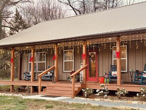 A wooden building with a porch decorated with lights and red bows, featuring a staircase and a door with a wreath. - Charming 2-BR farmhouse w/Hot Tub in delightful Bryson City, 2 min to downtown (Bryson City)