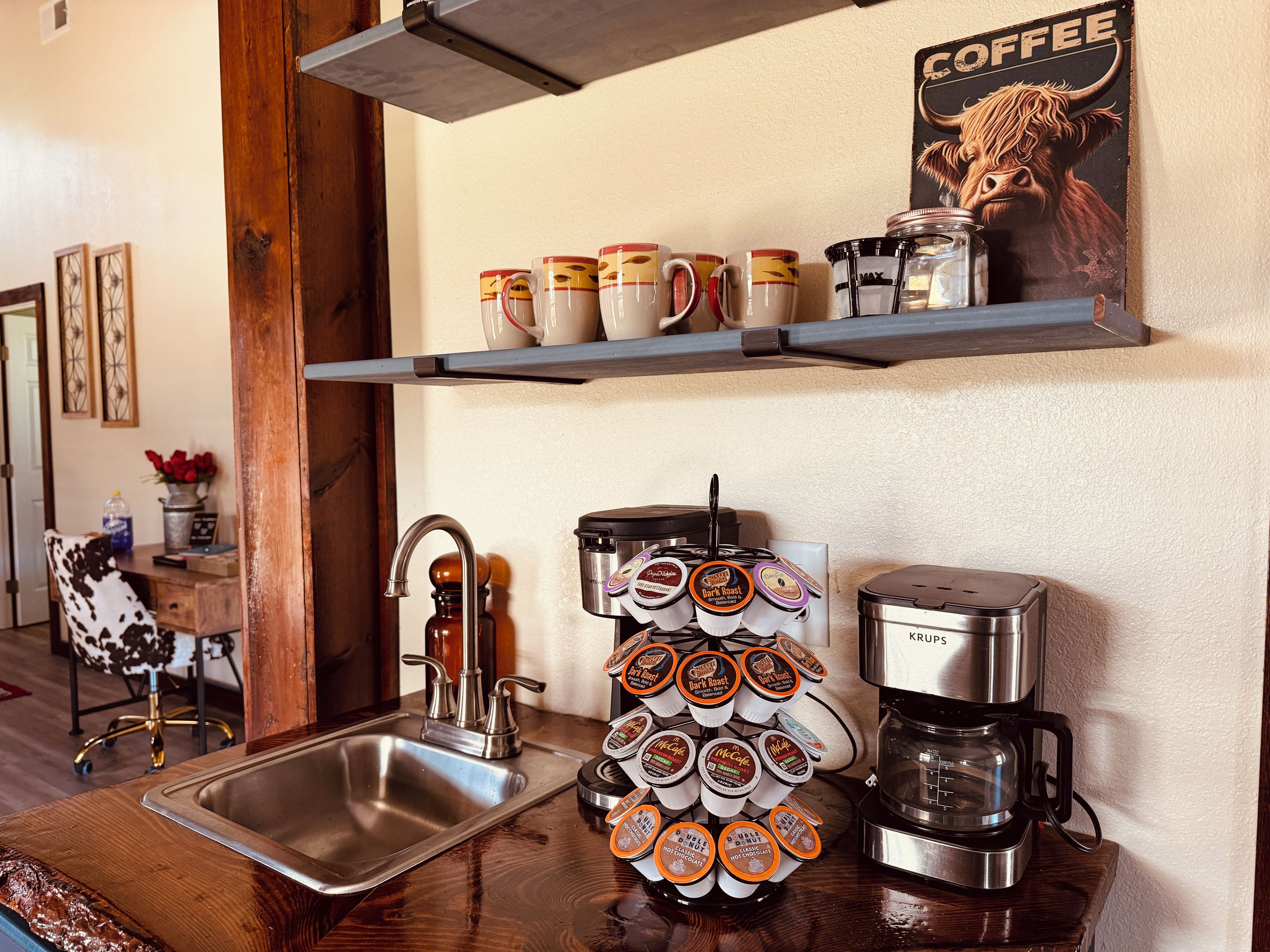 Cozinha com cafeteira, porta-xícaras e pôster com tema de café.