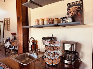 Una cocina con cafetera, un soporte para tazas de café y un póster con temática de café.