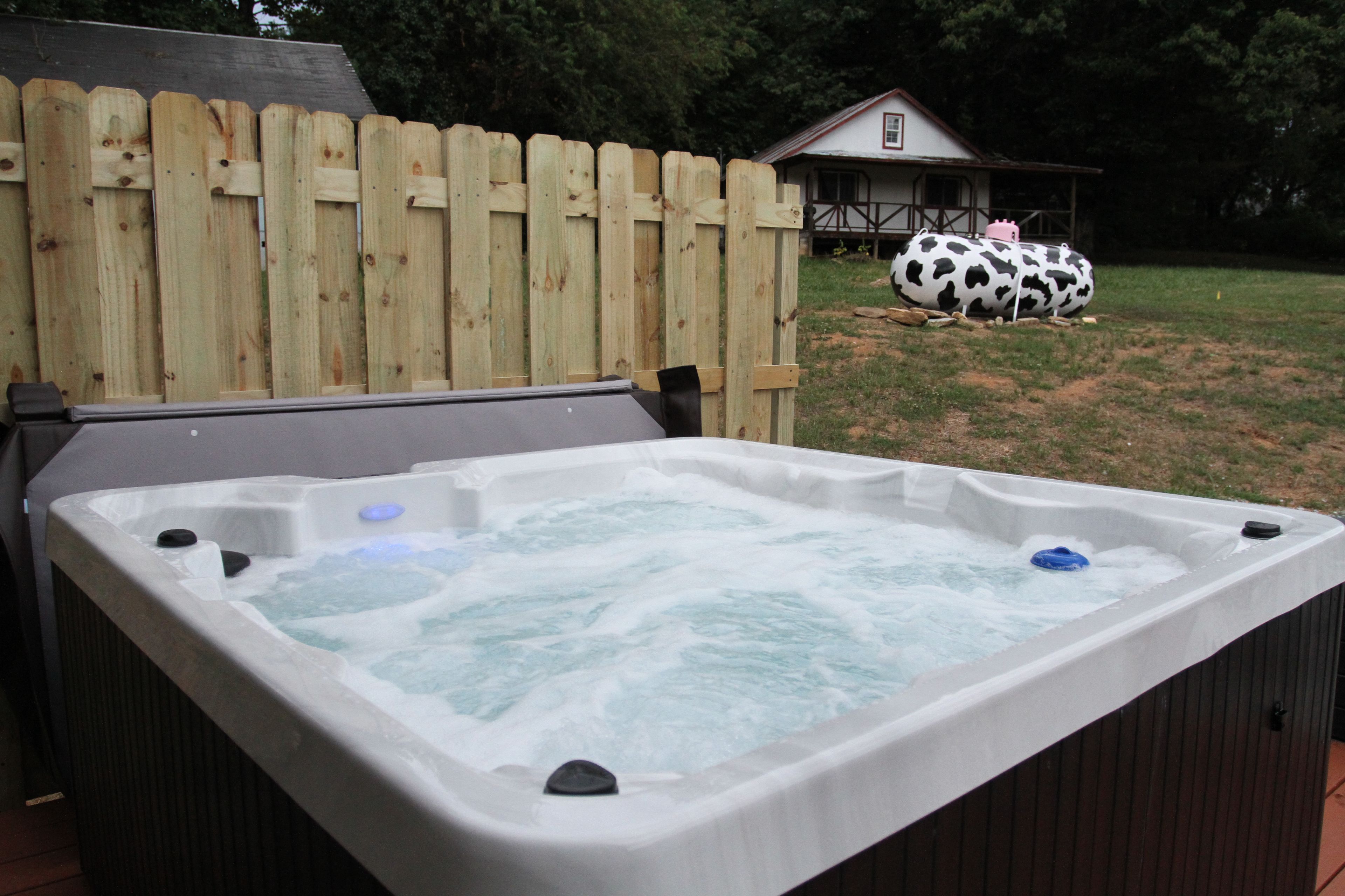 A hot tub with a wooden fence and a house in the background.