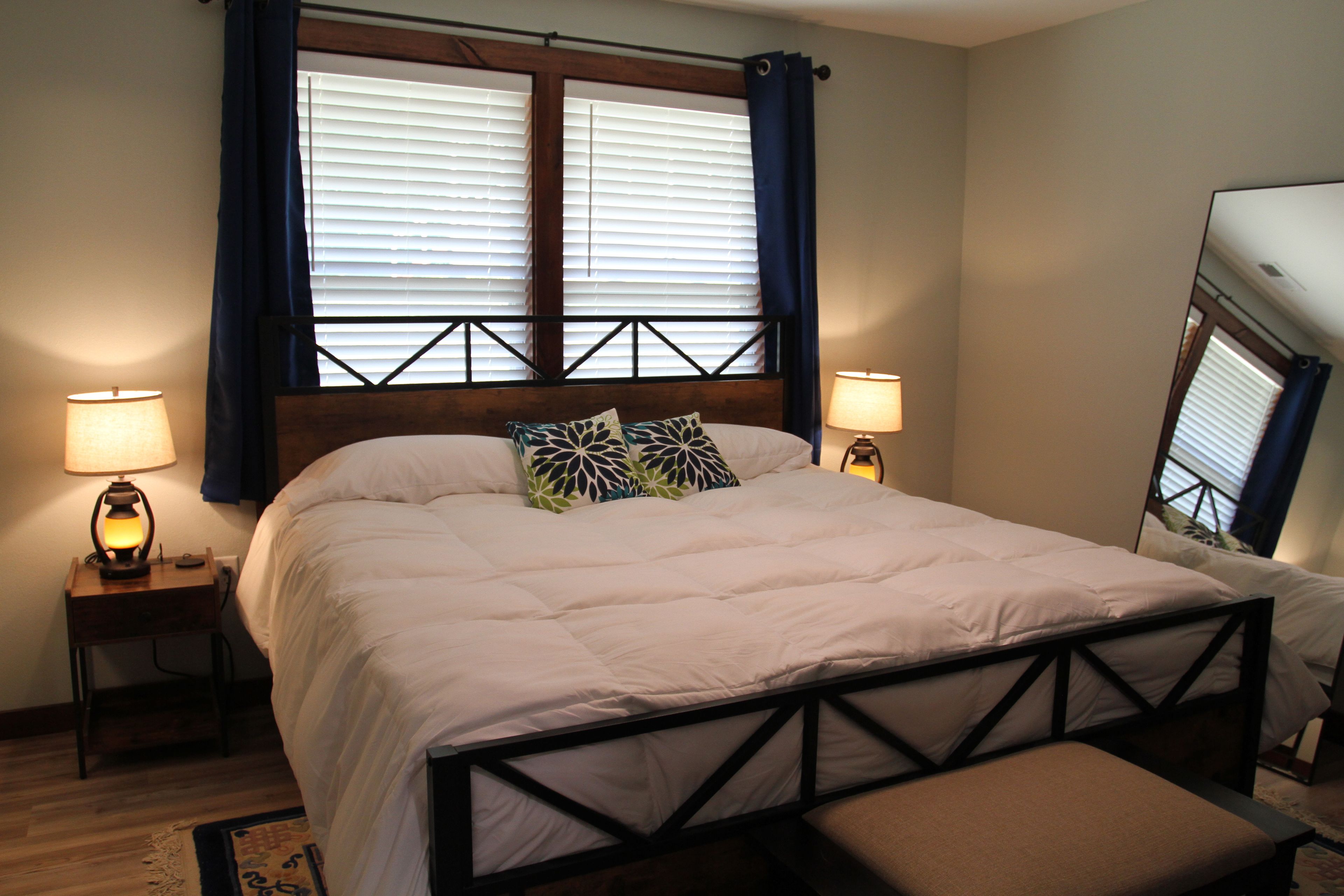 A bedroom with a bed, two bedside lamps, a window with blinds, and a bench.
