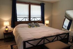 A bedroom with a bed, two bedside lamps, a window with blinds, and a view of a camper. - Charming 2-BR farmhouse w/Hot Tub in delightful Bryson City, 2 min to downtown (Bryson City)