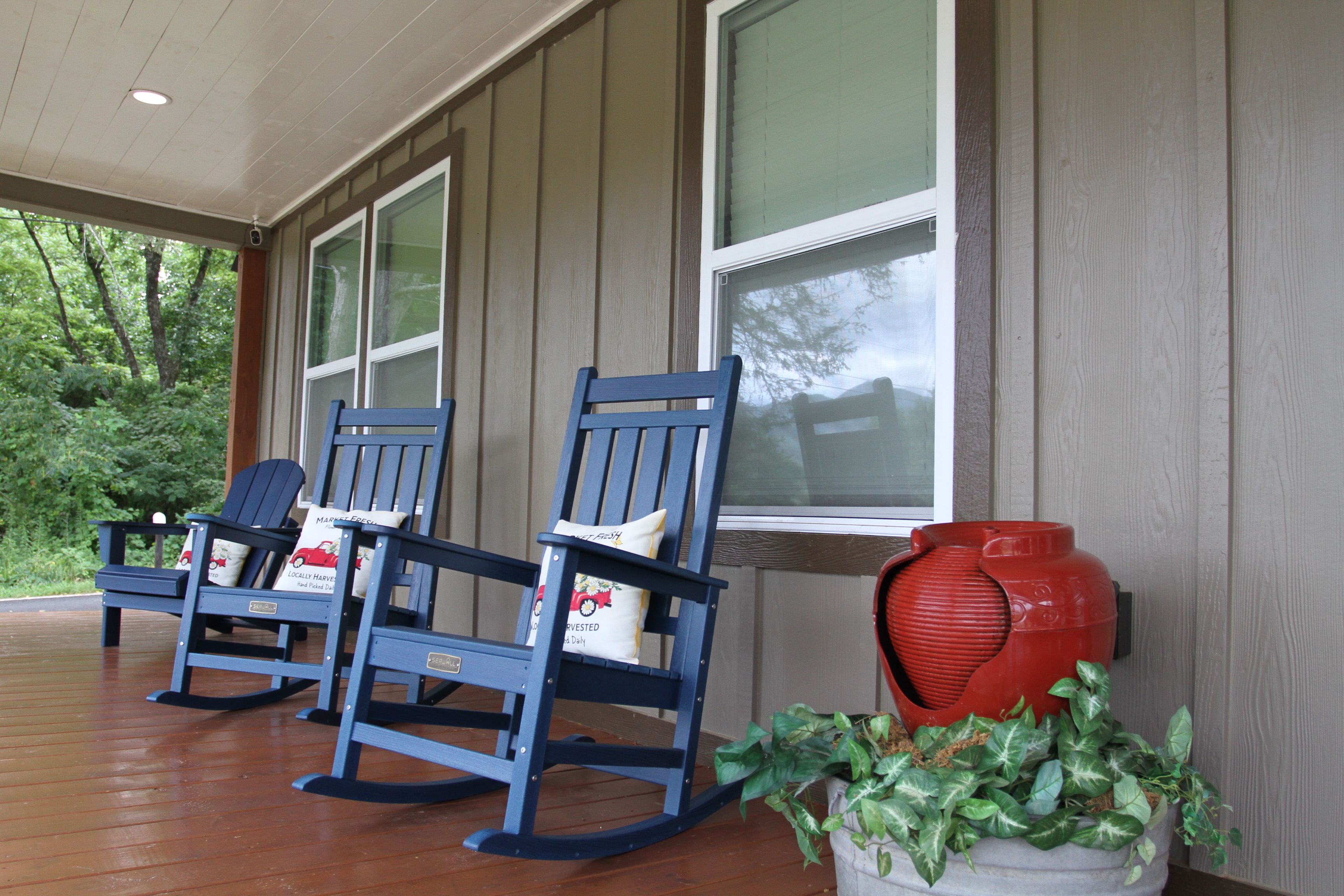 A porch with three rocking chairs and a red vase.
