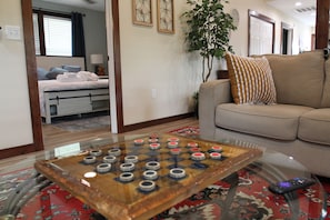 A living room with a glass coffee table, a sofa, a bed, and a plant.