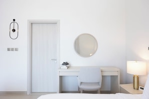 A hotel room with a bed, a desk with a chair, a round mirror, a bedside lamp, and a door. - Bloomfields Studio in Albatross 1 - YGC (Abu Dhabi)