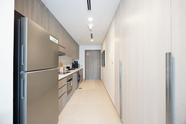 A modern kitchen with stainless steel appliances, wooden cabinets, and a tiled floor. - Bloomfields Studio in Albatross 1 - YGC (Abu Dhabi)