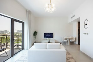A modern hotel room with a large bed, a TV, a dining area, and a balcony with a view of the city. - Bloomfields Studio in Albatross 1 - YGC (Abu Dhabi)