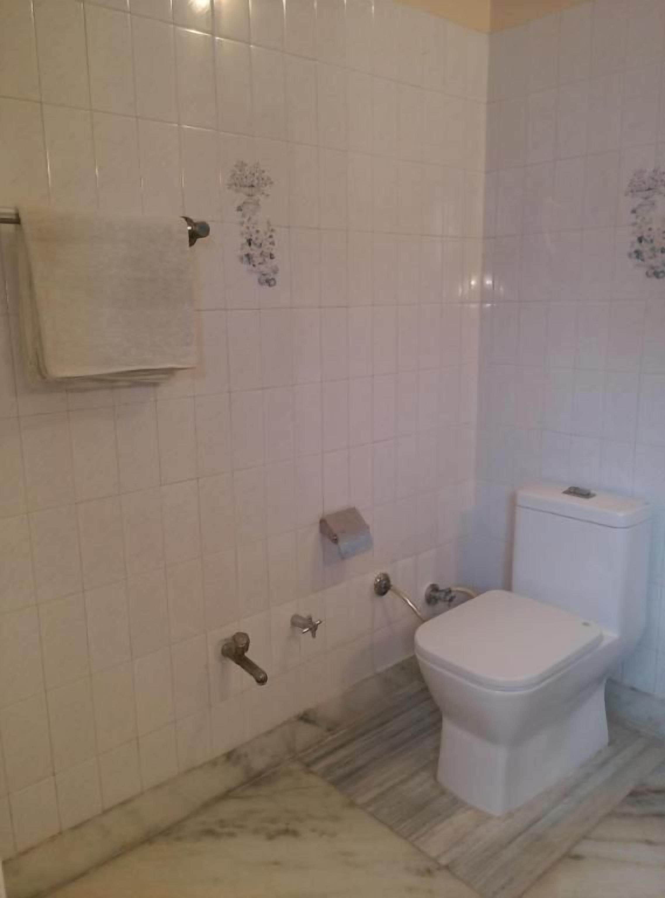 Un bagno con pareti piastrellate di bianco, un water, un portasciugamani e un pavimento in marmo.
