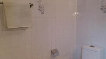 Un bagno con pareti piastrellate di bianco, un water, un portasciugamani e un pavimento in marmo.