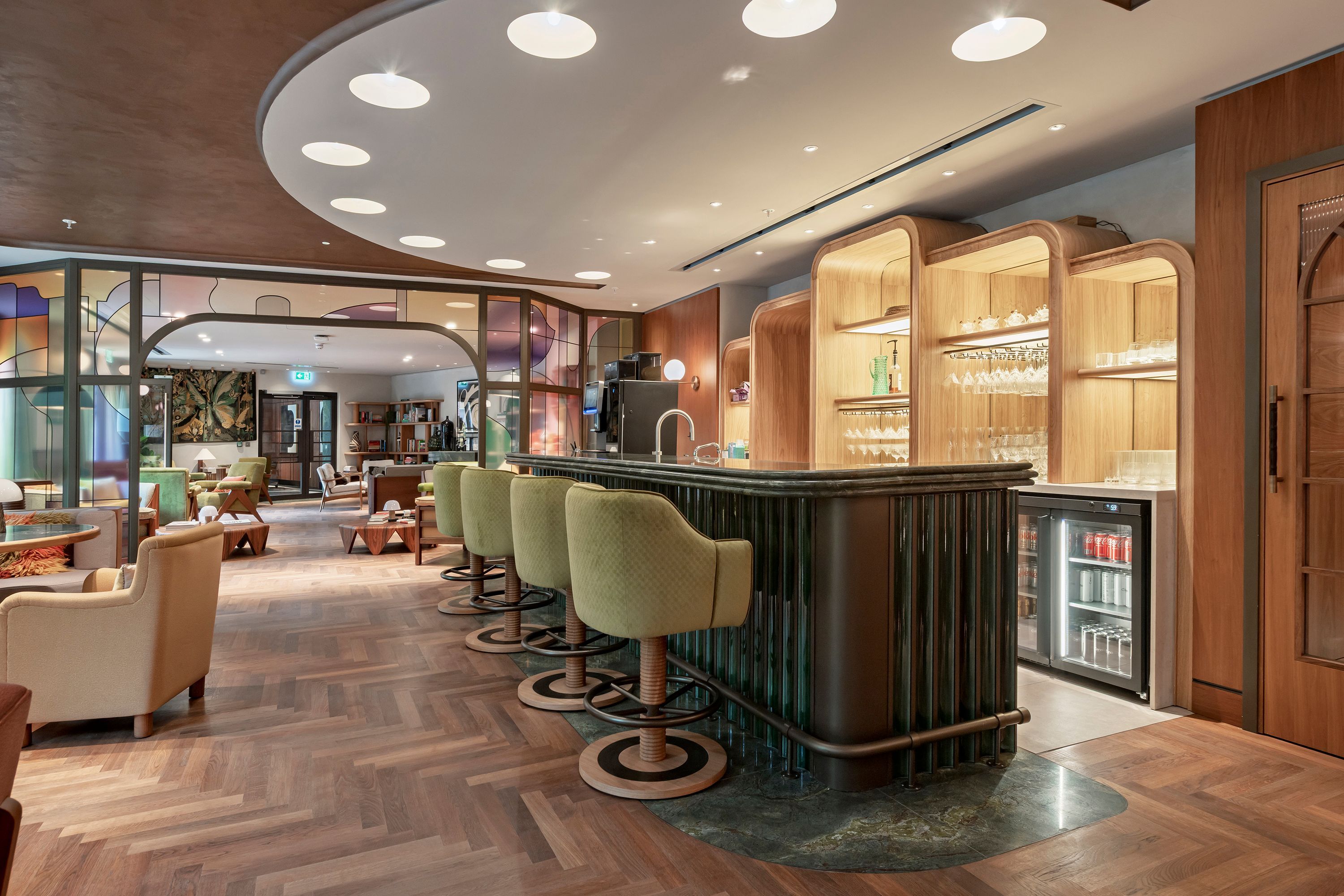 A modern bar area with a bar counter, stools, and a refrigerator stocked with beverages.