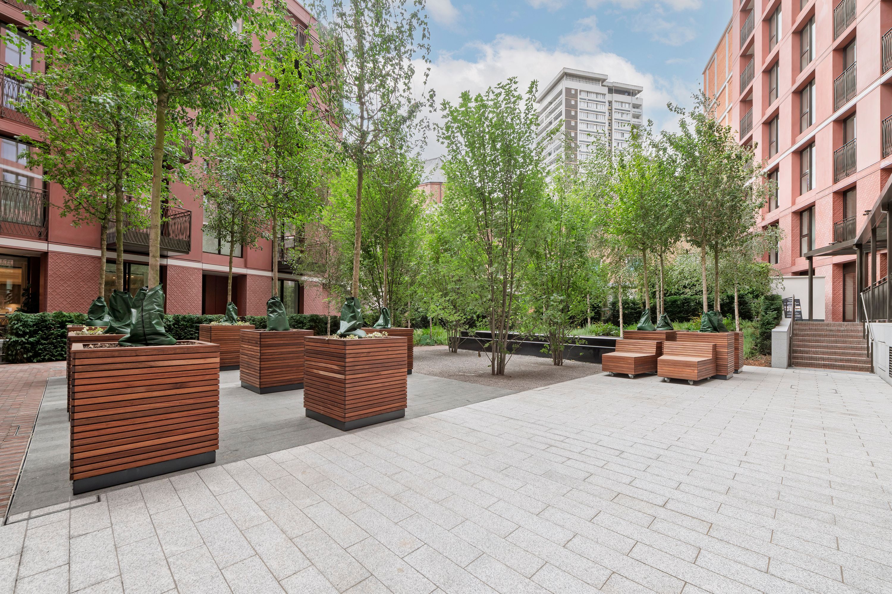 An outdoor courtyard with modern buildings, wooden planters, and a paved walkway.