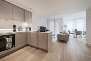 A modern kitchen with a central island, built-in appliances, and a dining area with a sofa and chairs. - Paddington Green by Veeve (London)
