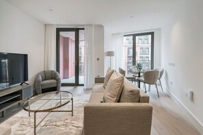 Una sala de estar moderna con un televisor de pantalla plana, un sillón estampado, un sofá color beige y una mesa de centro de vidrio.
