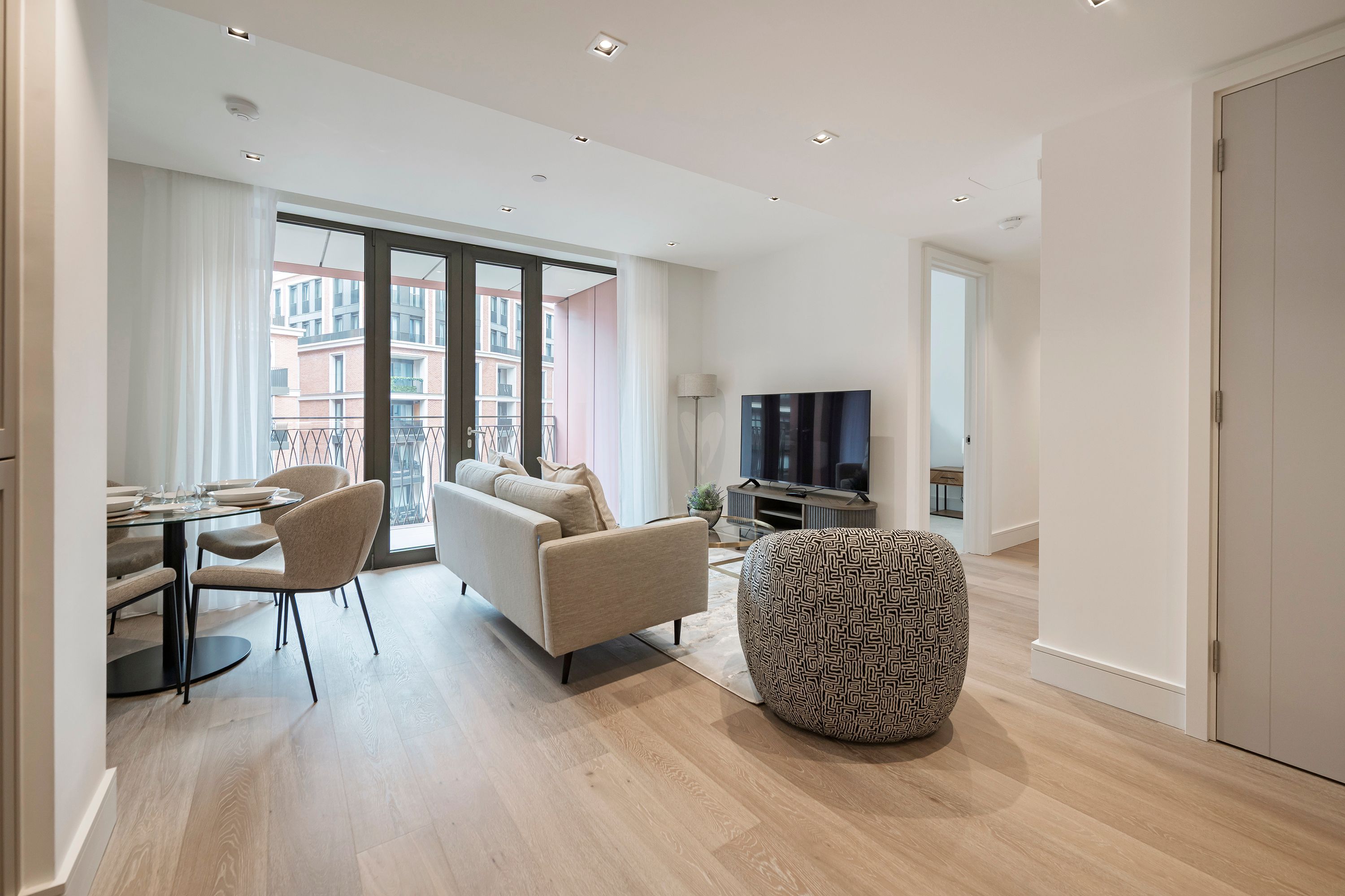 A modern living room with a sofa, chairs, a dining table, and a television.