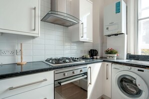 Une cuisine moderne avec des meubles blancs, une cuisinière à gaz, un four encastré, un four à micro-ondes et un lave-linge.