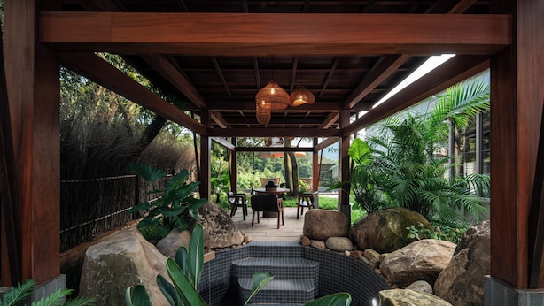 A covered outdoor seating area with a view of a lush garden, a hot tub, and a dining table with chairs. - Xiaoyin Cuiweiyang Resort (Shenzhen)