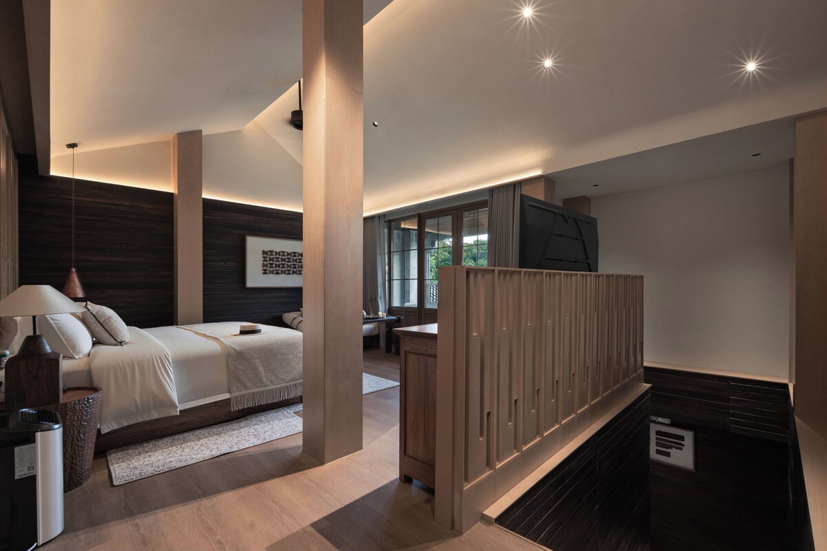 Quarto moderno com cama, mesa de cabeceira, abajur e vista para o exterior.