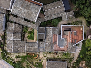Vista aérea de uma área residencial com vários edifícios, um pátio central com assentos e vegetação ao redor.