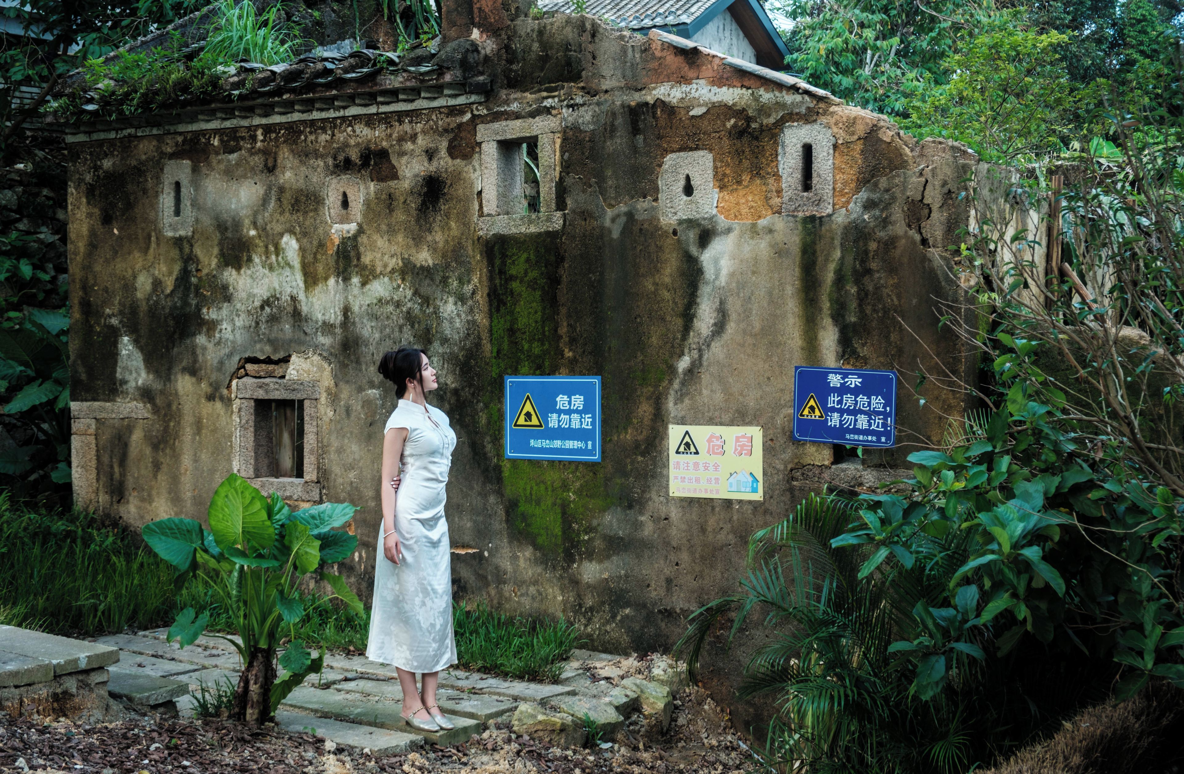 A woman standing in front of a dilapidated building with warning signs.