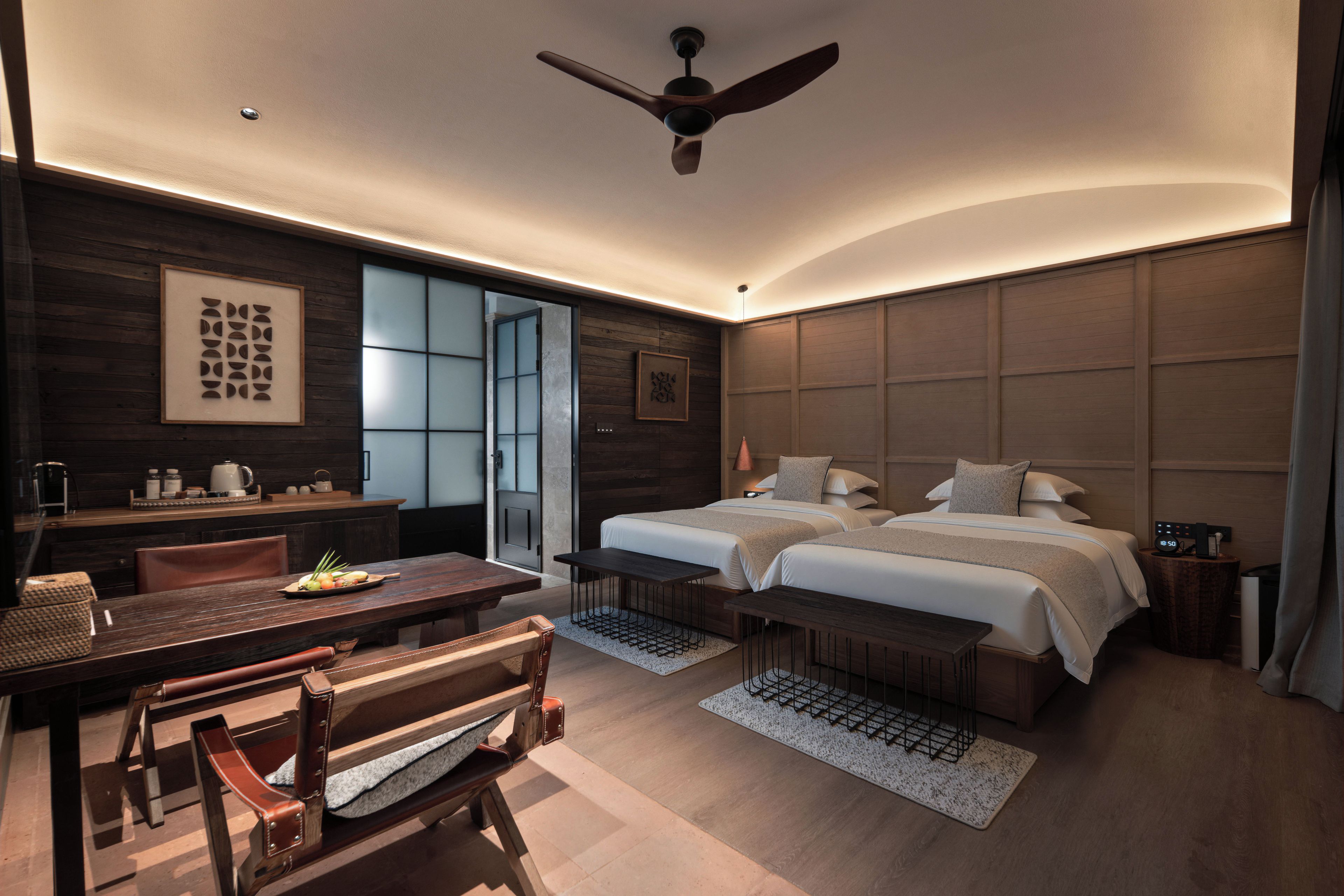 A modern hotel room with a bed, desk, chair, and a ceiling fan.