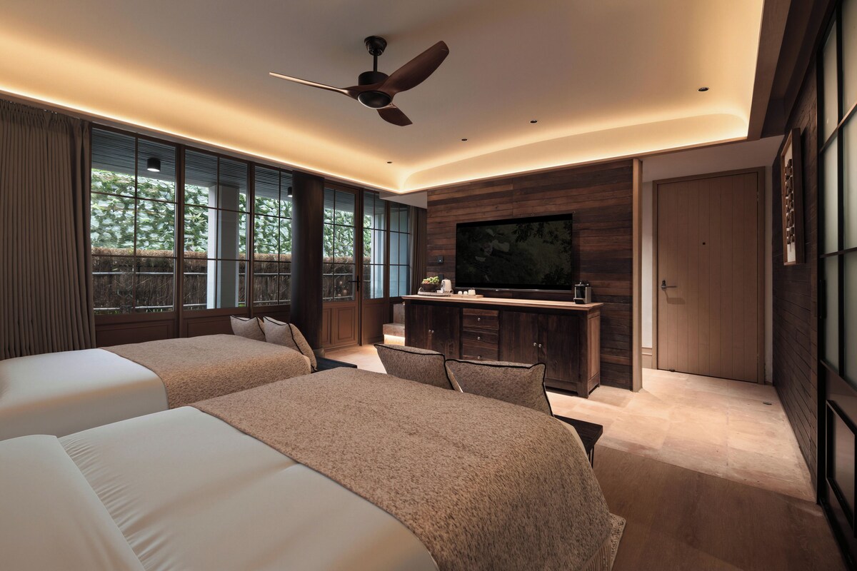 Quarto de hotel moderno com duas camas, uma escrivaninha e uma televisão.