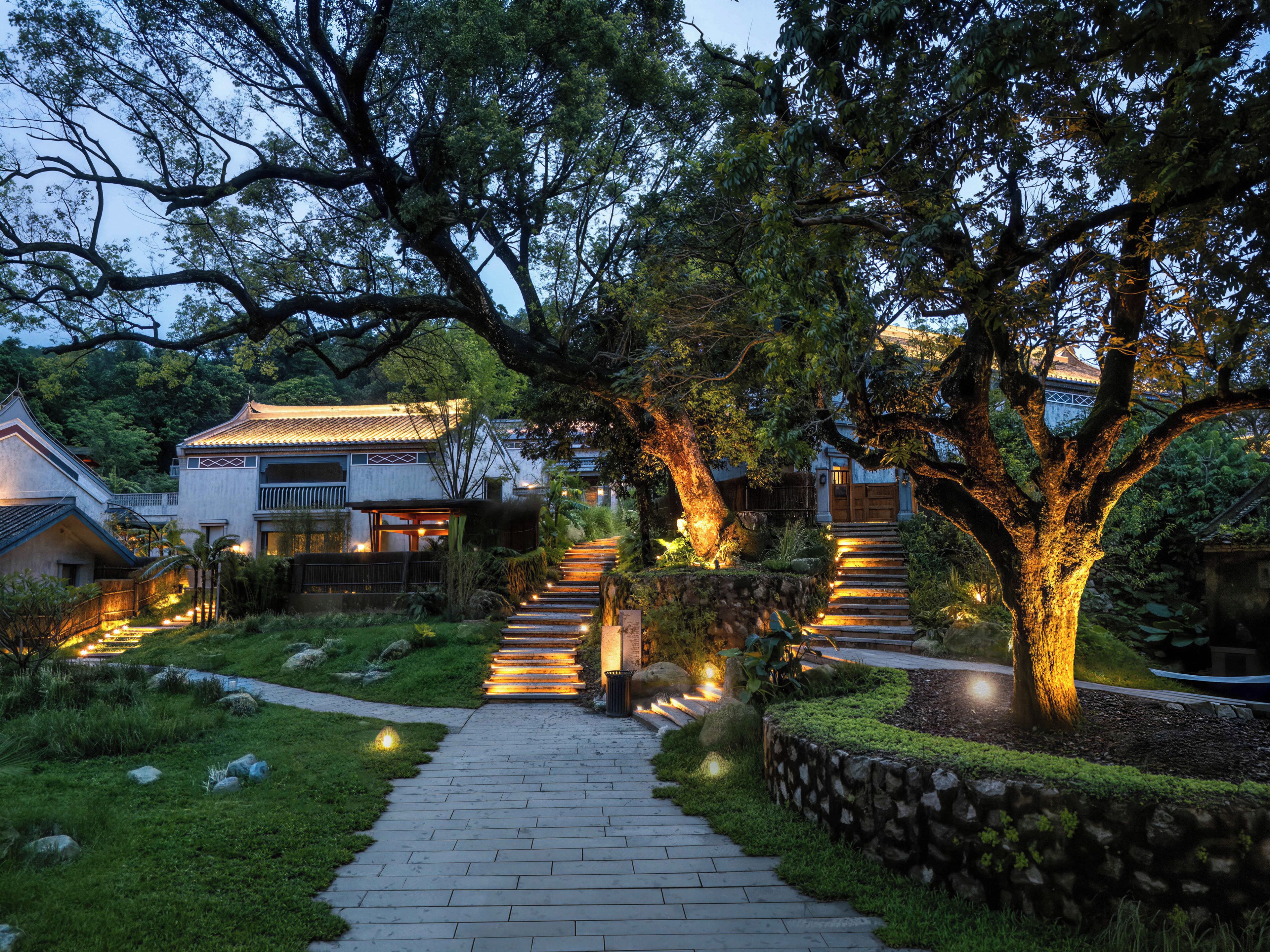 A pathway leading to a traditional-style building surrounded by trees and illuminated by warm lights.