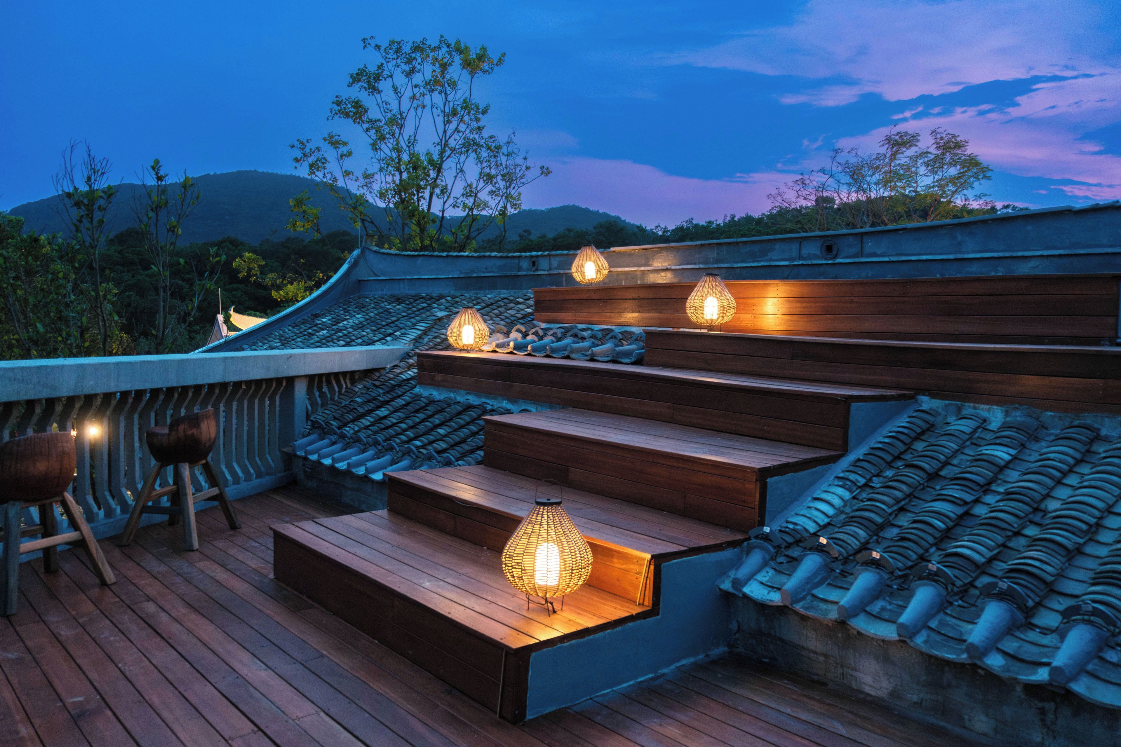 Una terraza de madera tradicional con asientos escalonados y faroles colgantes, con vistas a un paisaje montañoso.