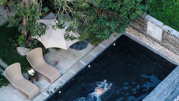 An aerial view of a swimming pool with a tiled edge, surrounded by lush greenery and a stone pathway.