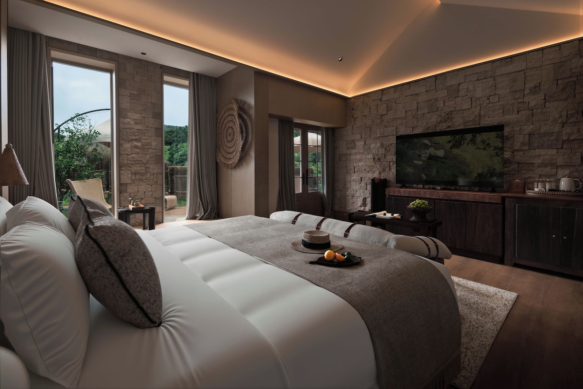 Quarto moderno com cama grande, televisão e parede de pedra.