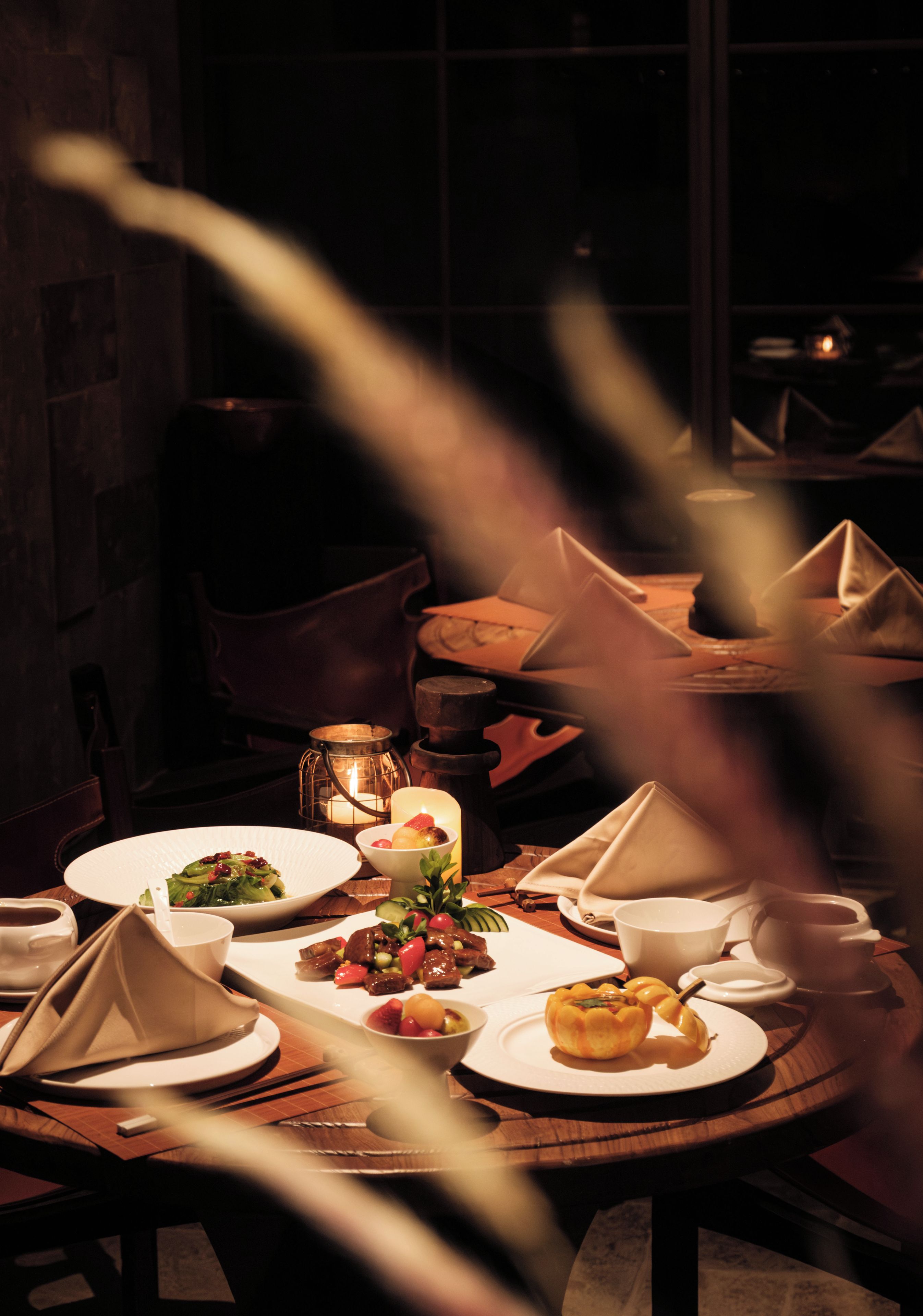 Un comedor con poca luz, con una mesa dispuesta para una comida, incluyendo platos, tazones y una vela.