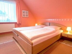 Ein Einzelbett mit Holzrahmen, ein Nachttisch mit Lampe, ein Fenster mit Vorhängen und eine Heizung.