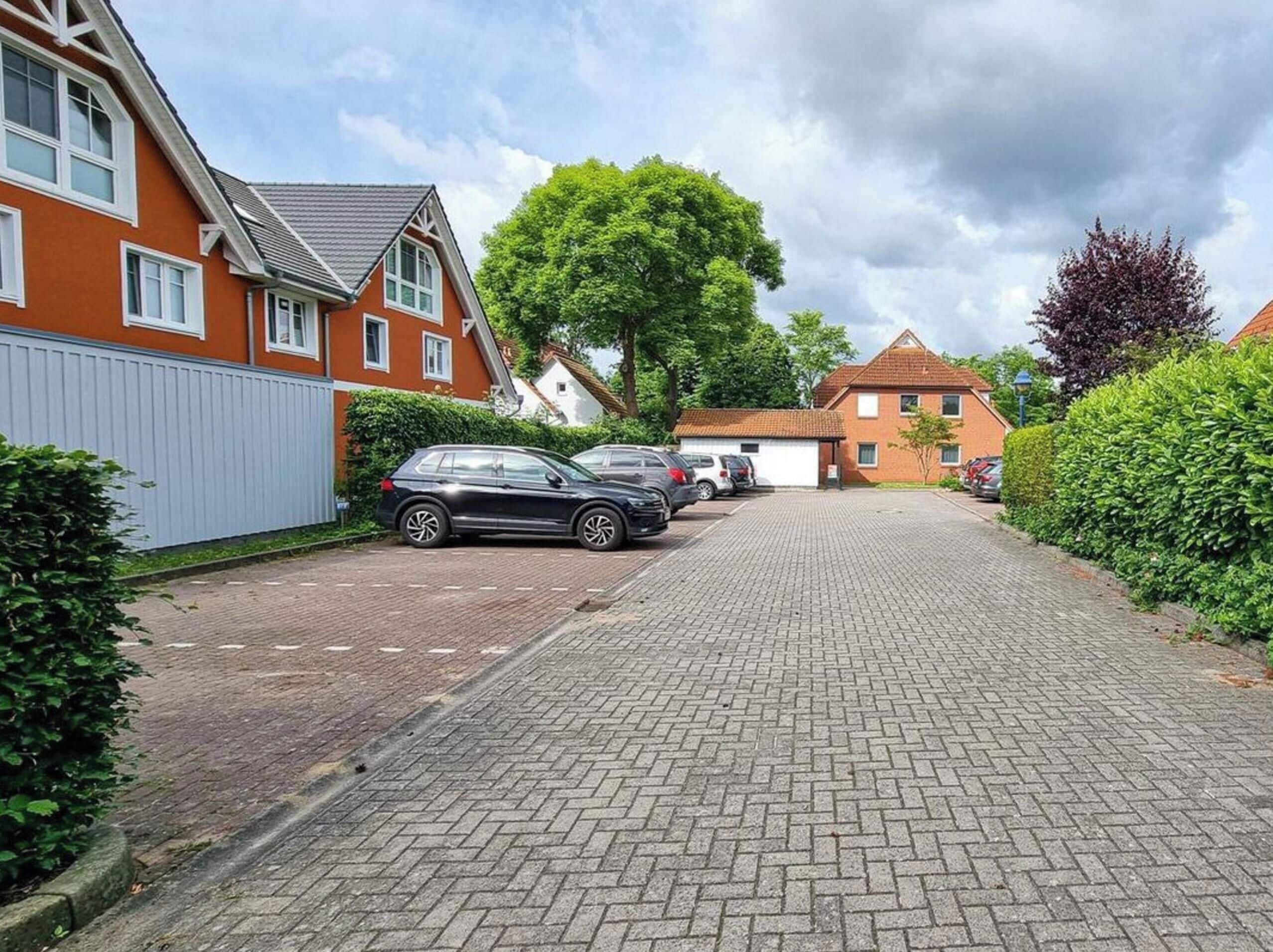 A residential street with houses, parked cars, and a paved walkway.