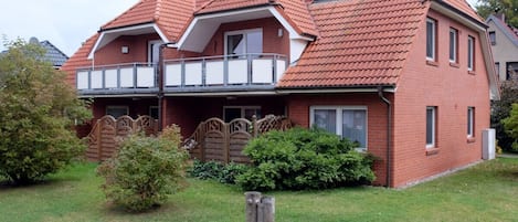 A two-story house with a red-tiled roof, a balcony, and a well-maintained front yard with a wooden fence and a stone pillar.