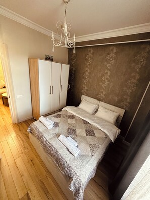 A bedroom with a bed, a wardrobe, a chandelier, and a patterned headboard. - Modern Apartment with Balcony & WiFi (T'bilisi)