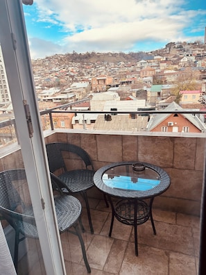 A balcony with two wicker chairs and a small round table, overlooking a densely packed urban area with various buildings. - Modern Apartment with Balcony & WiFi (T'bilisi)