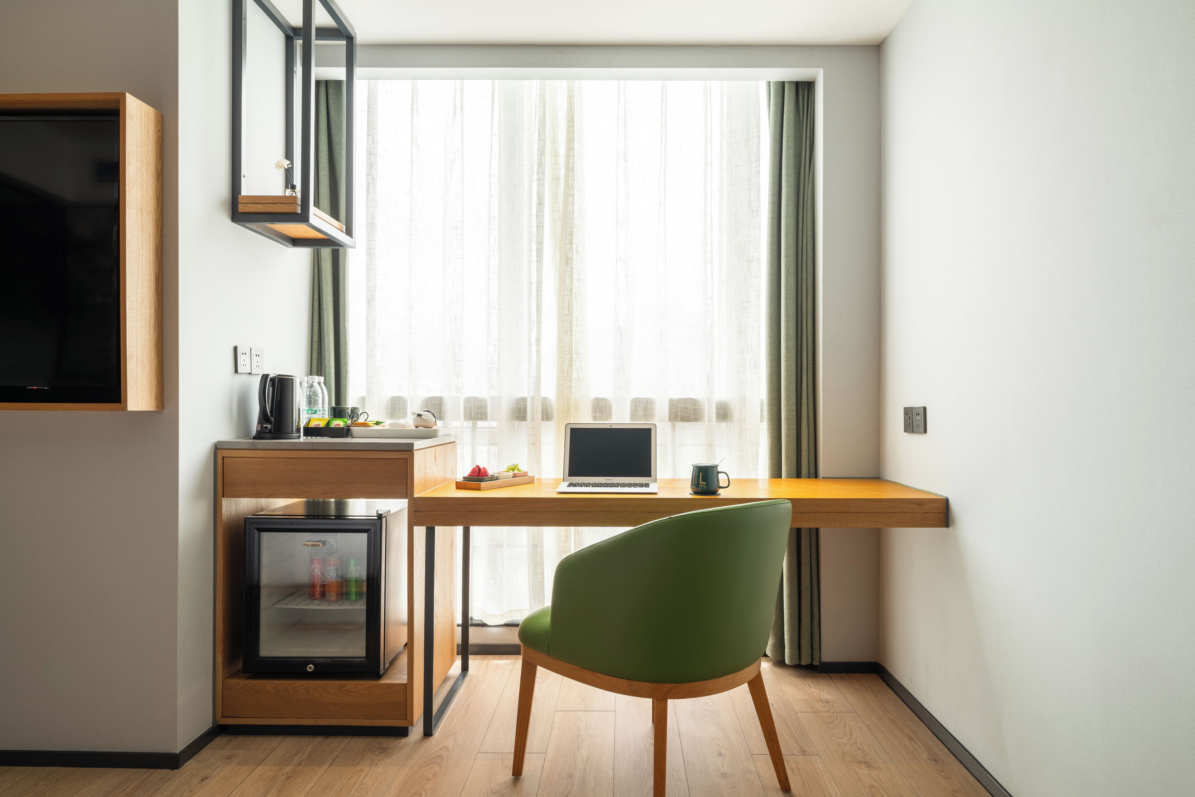 A compact workspace with a laptop, a green chair, and a small refrigerator.