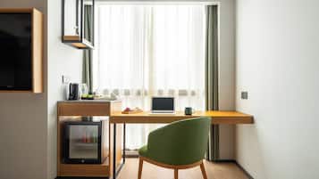 Un espacio de trabajo reducido con una computadora portátil, una silla verde y un refrigerador pequeño.