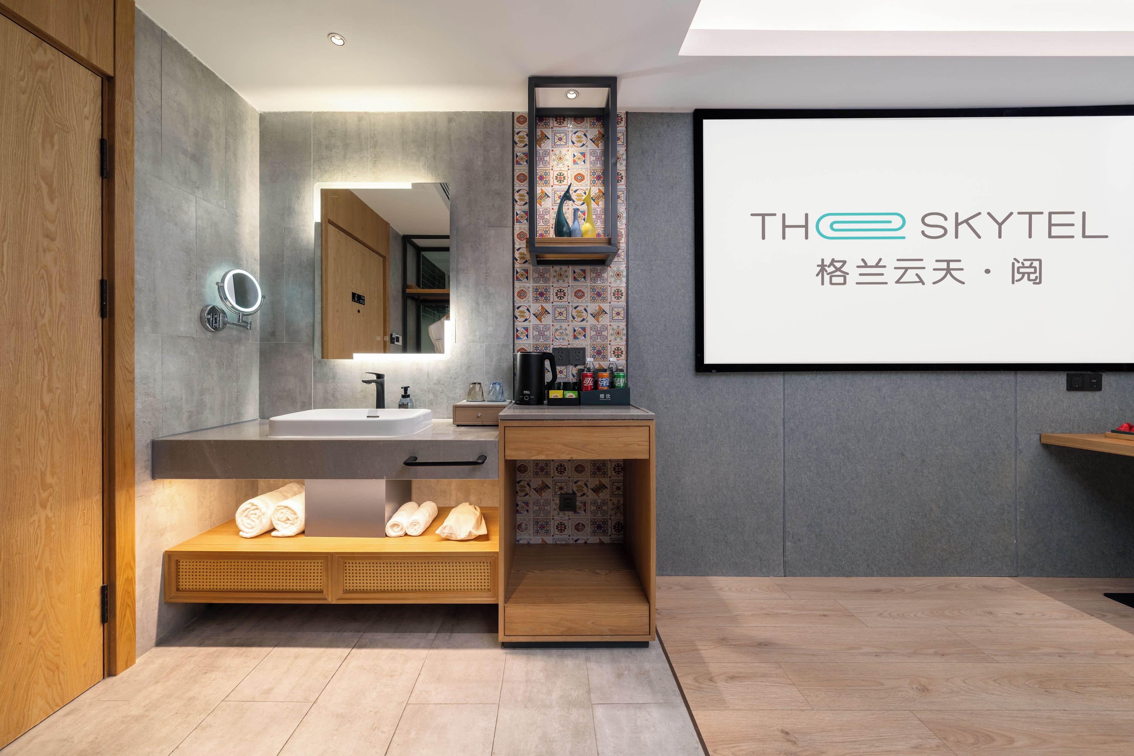 A modern bathroom with a large mirror, a sink, and a shower area. There is a wooden cabinet with towels and toiletries.